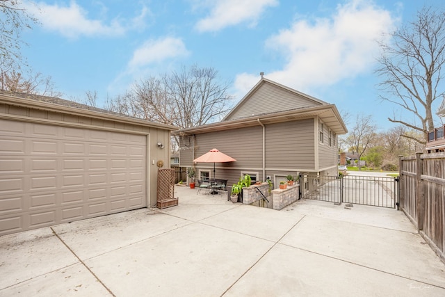 view of property exterior with concrete driveway, a gate, an outbuilding, fence, and a garage