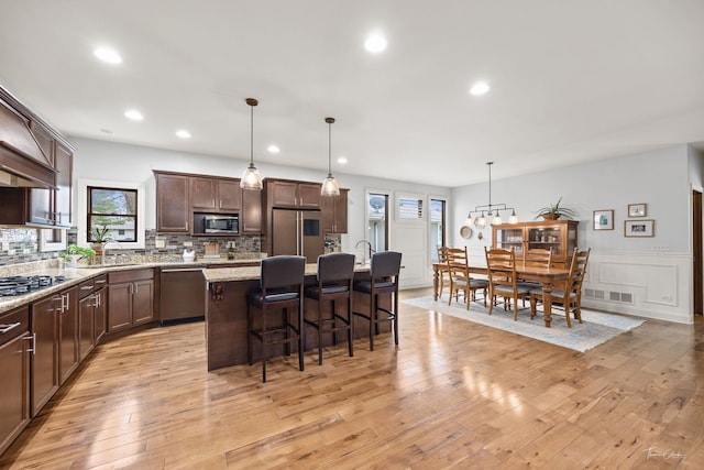 kitchen featuring stainless steel appliances, dark brown cabinets, a kitchen bar, decorative backsplash, and a kitchen island