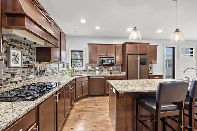 kitchen with custom exhaust hood, a sink, a breakfast bar area, light wood-type flooring, and stainless steel appliances