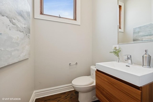 half bathroom featuring toilet, vanity, wood finished floors, and baseboards