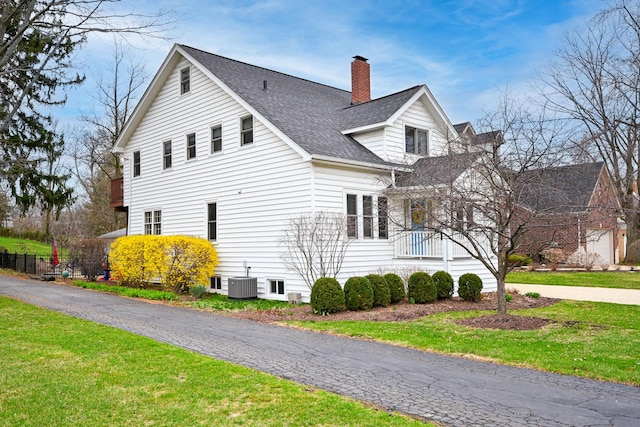 view of side of home featuring a chimney, roof with shingles, a yard, and cooling unit