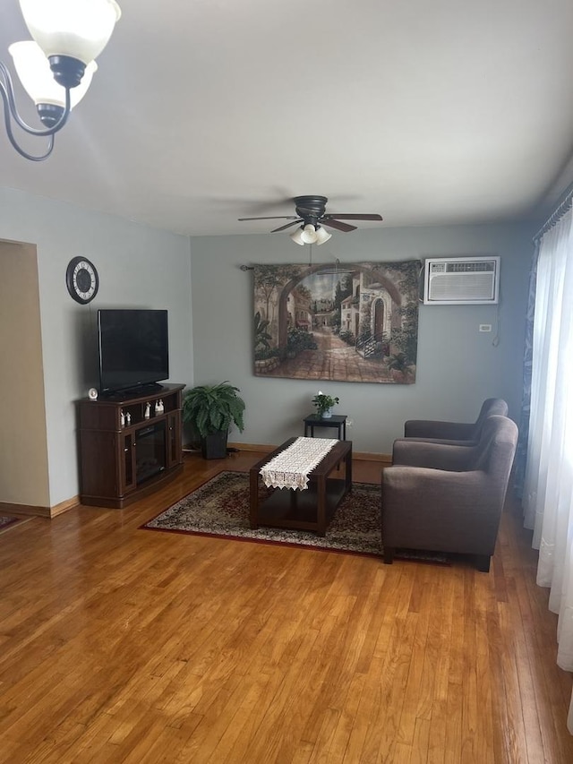 living area with wood-type flooring, a ceiling fan, a wall unit AC, and baseboards