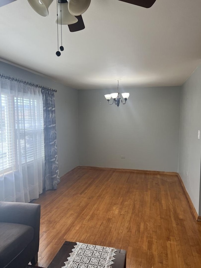unfurnished room with a chandelier, a ceiling fan, light wood-type flooring, and baseboards