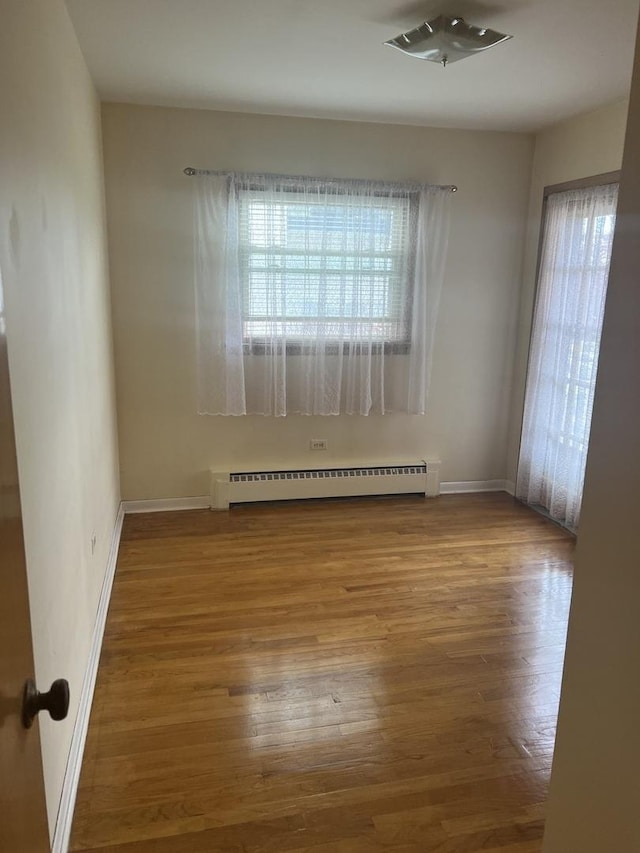 empty room featuring a baseboard radiator, plenty of natural light, wood finished floors, and baseboards