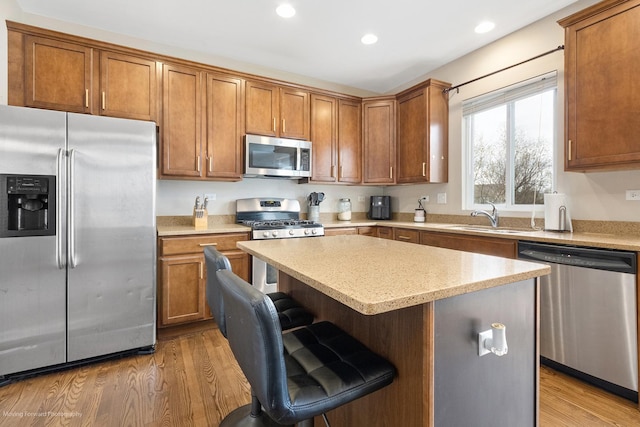 kitchen featuring stainless steel appliances, a center island, a sink, recessed lighting, and brown cabinetry