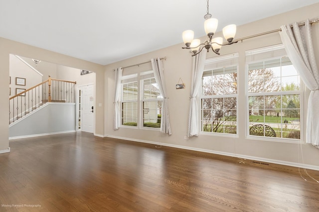 unfurnished living room featuring baseboards, wood finished floors, a notable chandelier, and stairway