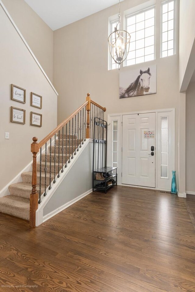 foyer entrance with a chandelier, stairway, a towering ceiling, and wood finished floors