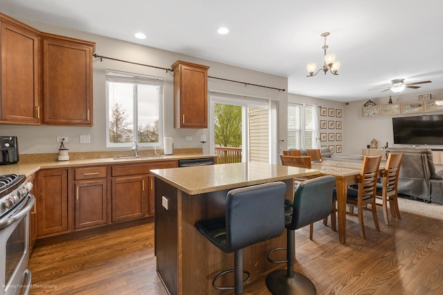 kitchen with a kitchen breakfast bar, a sink, wood finished floors, brown cabinetry, and light countertops