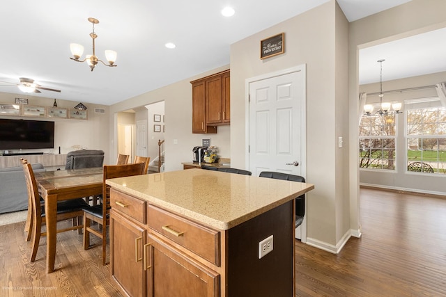 kitchen featuring light stone countertops, a center island, open floor plan, dark wood-style flooring, and ceiling fan with notable chandelier