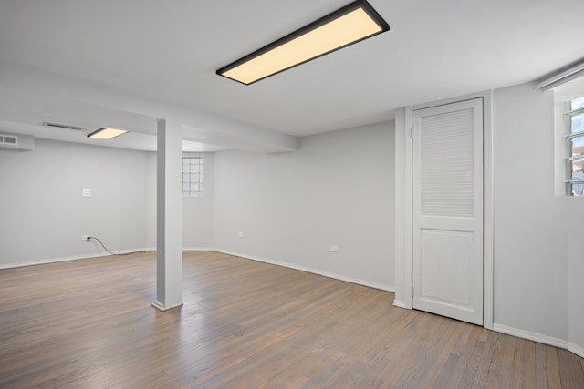 basement featuring baseboards, wood finished floors, visible vents, and plenty of natural light