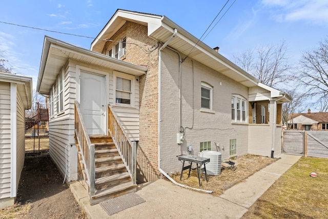 back of property featuring brick siding, entry steps, central AC, and fence
