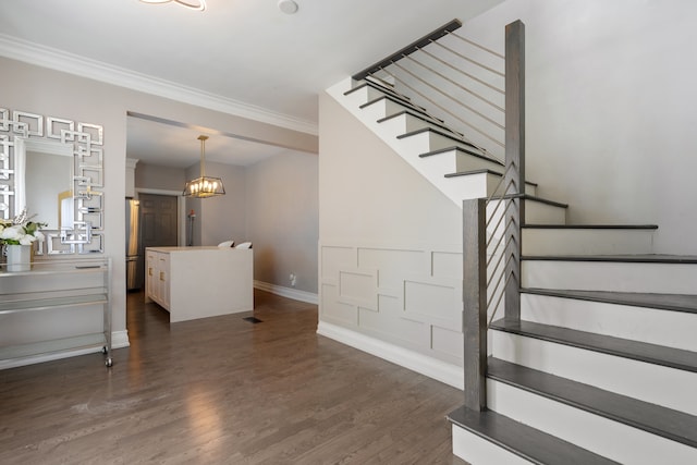 stairway featuring baseboards, wood finished floors, an inviting chandelier, and crown molding
