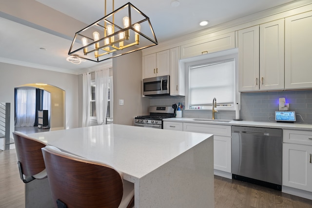 kitchen featuring stainless steel appliances, ornamental molding, a sink, arched walkways, and a center island