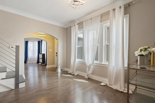 interior space featuring arched walkways, baseboards, wood finished floors, stairway, and crown molding