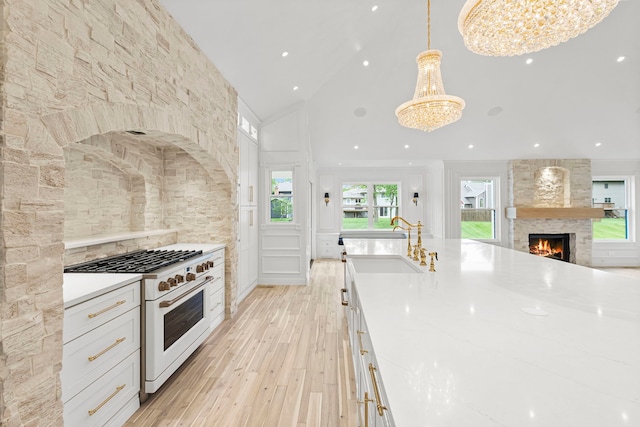 1004 Golden Ave, Woodstock, IL 60098 - kitchen featuring light wood finished floors, a stone fireplace, a sink, a chandelier, and white range with gas cooktop