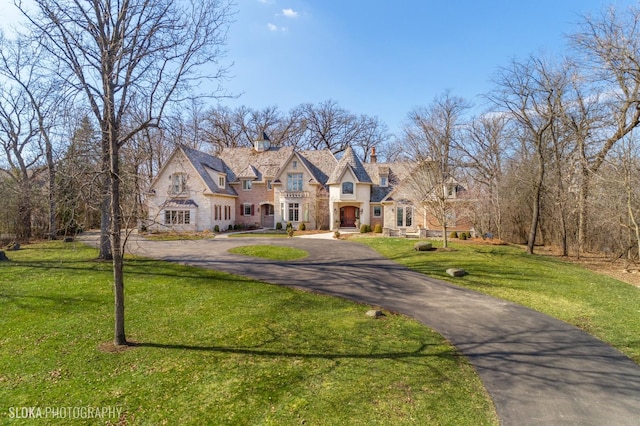 french provincial home with stone siding, a front lawn, and aphalt driveway