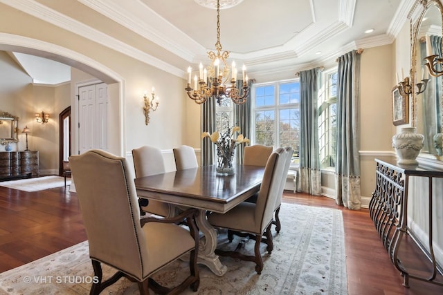 dining area with a raised ceiling, wood finished floors, arched walkways, crown molding, and a chandelier