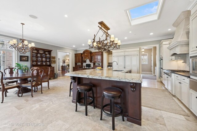 kitchen with a large island with sink, an inviting chandelier, a sink, crown molding, and custom range hood
