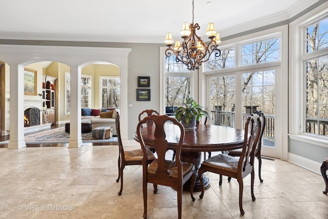 dining space featuring a notable chandelier, ornamental molding, a warm lit fireplace, and a healthy amount of sunlight