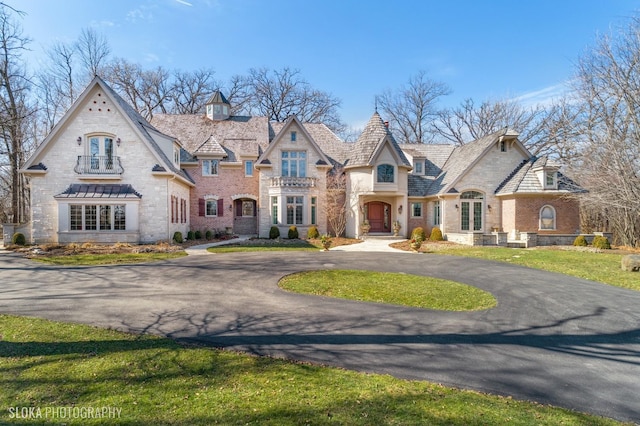 french country inspired facade featuring french doors, stone siding, a front yard, and curved driveway