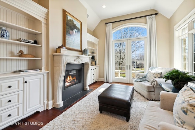 living area featuring built in shelves, french doors, a premium fireplace, lofted ceiling, and dark wood-type flooring