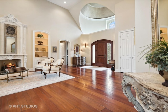 entryway featuring wood-type flooring, arched walkways, a high end fireplace, and high vaulted ceiling