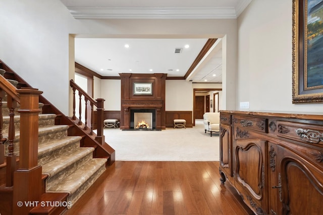 entrance foyer with hardwood / wood-style floors, stairway, ornamental molding, wainscoting, and a large fireplace