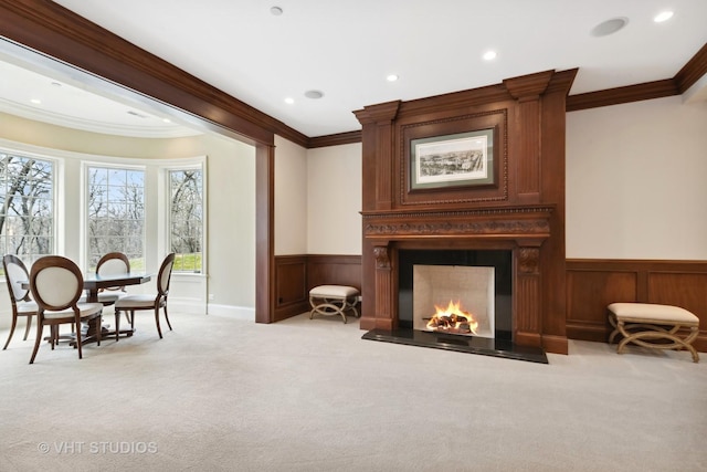 sitting room featuring recessed lighting, light colored carpet, crown molding, wainscoting, and a large fireplace