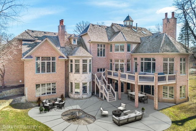 rear view of property with a chimney, brick siding, an outdoor living space, and a patio area