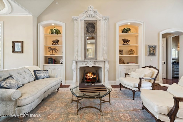 living room with arched walkways, a premium fireplace, wood finished floors, and built in shelves