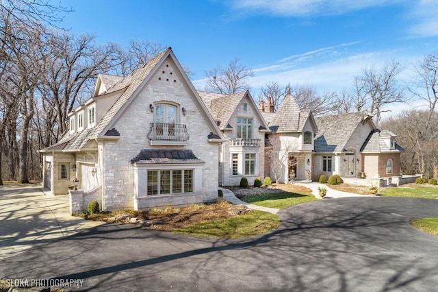 view of front of house featuring driveway, stone siding, and a balcony