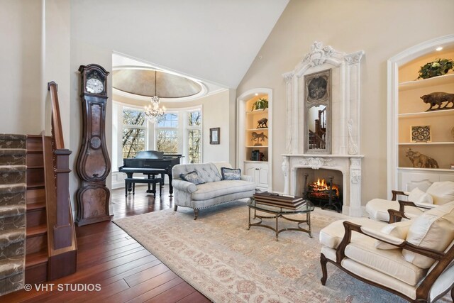 living area with an inviting chandelier, built in shelves, a premium fireplace, hardwood / wood-style floors, and high vaulted ceiling