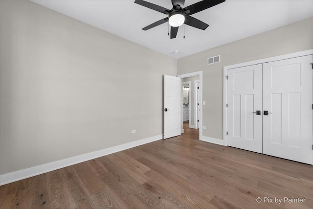 unfurnished bedroom with wood finished floors, a closet, ceiling fan, baseboards, and visible vents