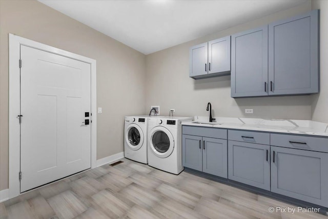 laundry room featuring a sink, separate washer and dryer, light wood-style floors, cabinet space, and baseboards
