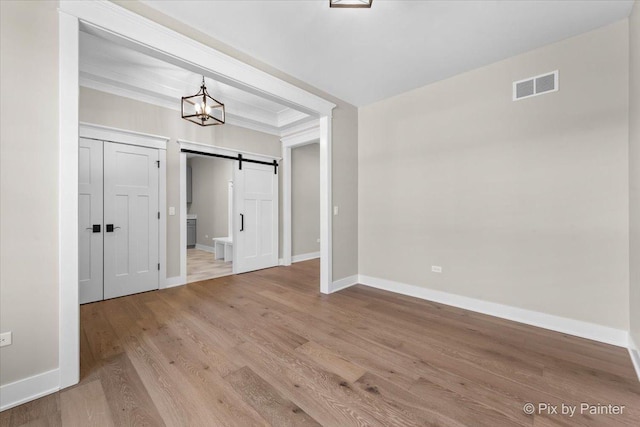 unfurnished room with a barn door, baseboards, visible vents, an inviting chandelier, and wood finished floors