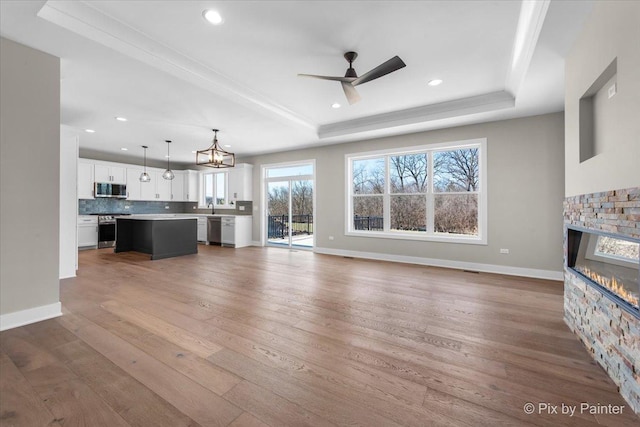 unfurnished living room with a fireplace, recessed lighting, wood finished floors, and a raised ceiling