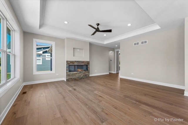 unfurnished living room featuring wood finished floors, ceiling fan, a fireplace, baseboards, and a raised ceiling