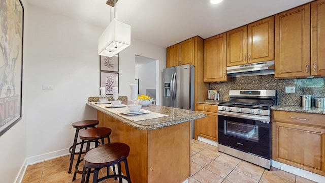 7350 N Karlov Ave, Lincolnwood, IL 60712 - kitchen with appliances with stainless steel finishes, under cabinet range hood, a kitchen breakfast bar, light tile patterned flooring, and brown cabinetry