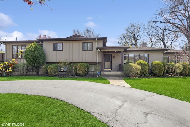 tri-level home featuring a chimney, a front lawn, and brick siding