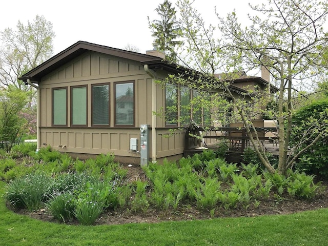 view of side of property with board and batten siding, a wooden deck, and a chimney