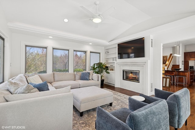 living room featuring ceiling fan, dark wood-style flooring, built in features, lofted ceiling, and a glass covered fireplace