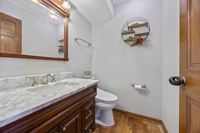 bathroom featuring baseboards, toilet, ornamental molding, wood finished floors, and vanity