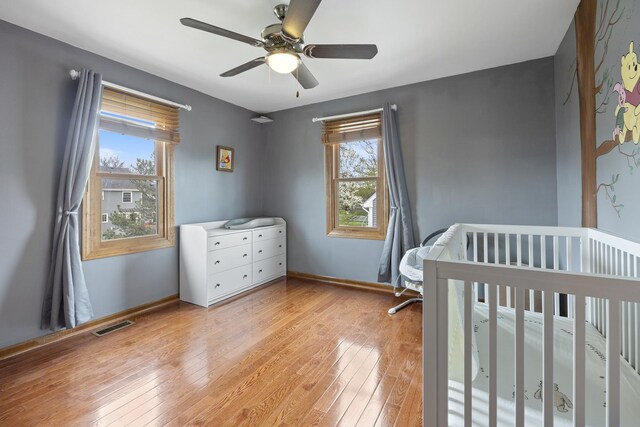 bedroom with light wood-style floors, ceiling fan, visible vents, baseboards, and a crib