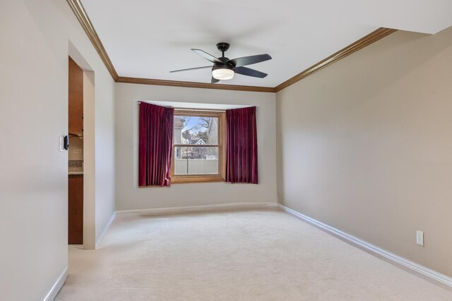 spare room featuring a ceiling fan, ornamental molding, baseboards, and light carpet