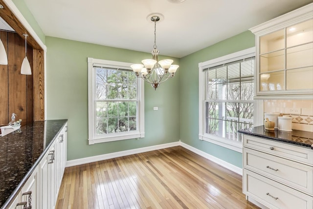 unfurnished dining area with baseboards, an inviting chandelier, and light wood-type flooring