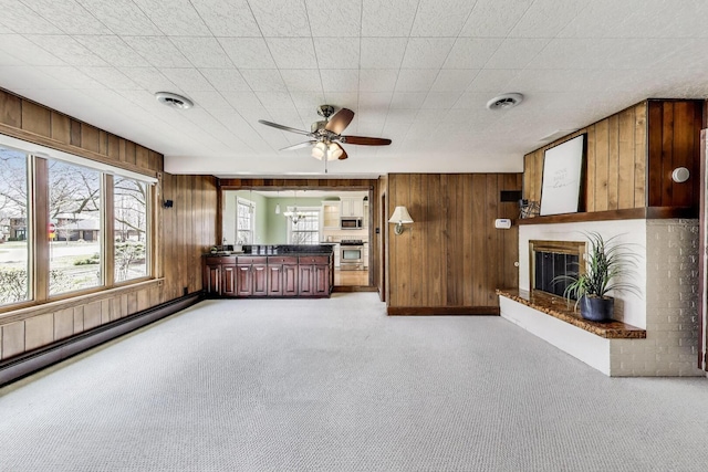 unfurnished living room with wooden walls, visible vents, a ceiling fan, light carpet, and a glass covered fireplace