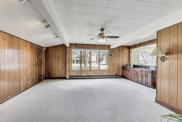 unfurnished living room with wooden walls, plenty of natural light, and ceiling fan