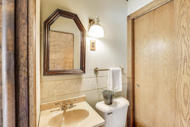 bathroom featuring tile walls, toilet, and a sink