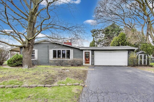 ranch-style house featuring a chimney, an attached garage, an outdoor structure, a shed, and aphalt driveway