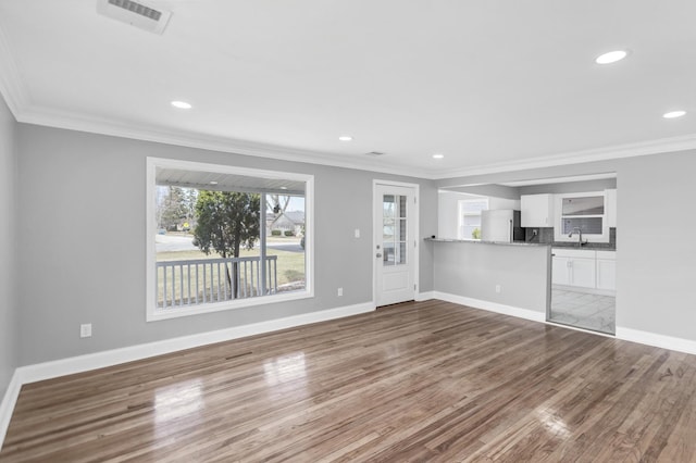 unfurnished living room with wood finished floors, visible vents, a sink, and crown molding